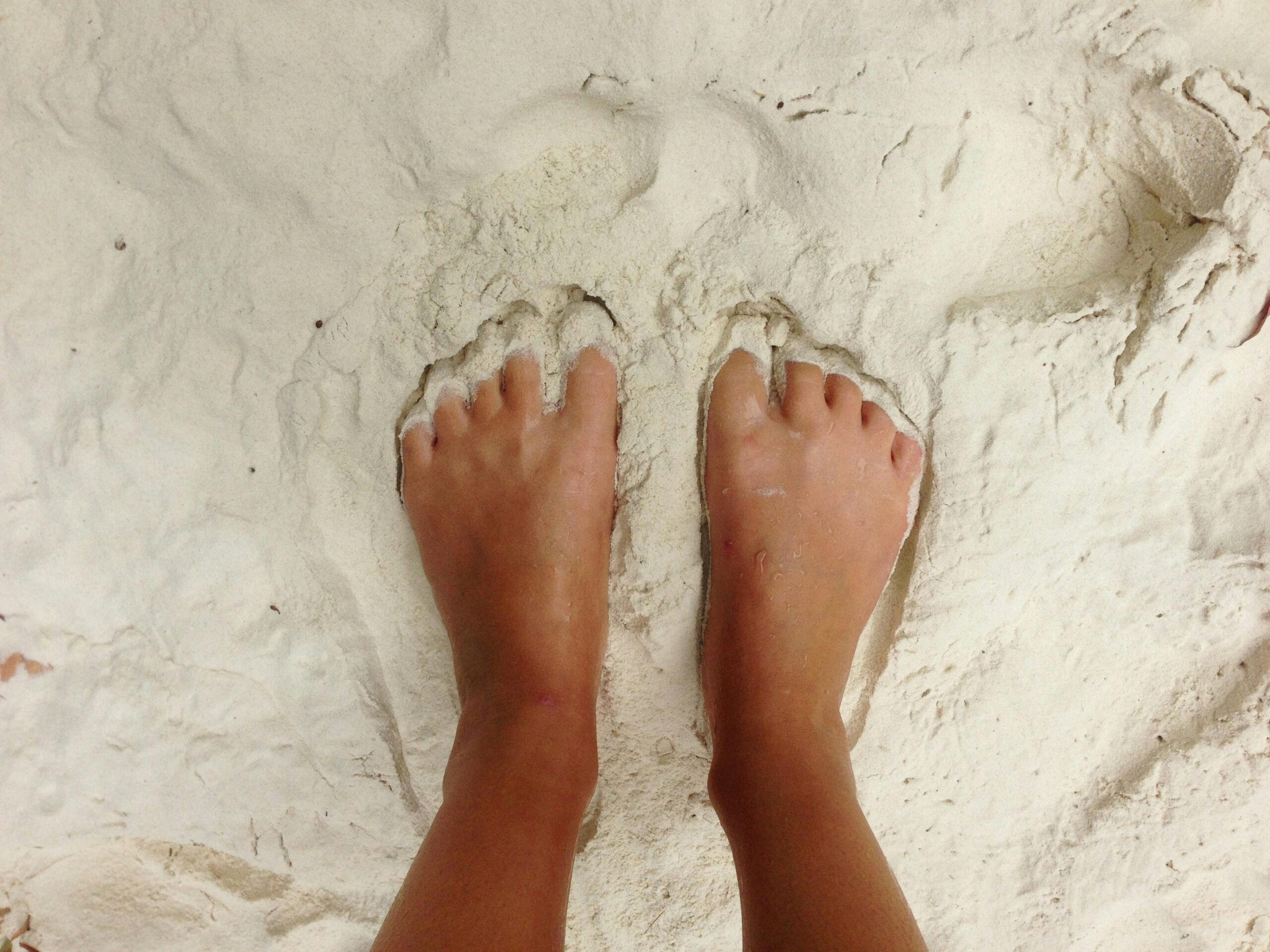Close-up of bare feet immersed in white sand, evoking a sense of relaxation.