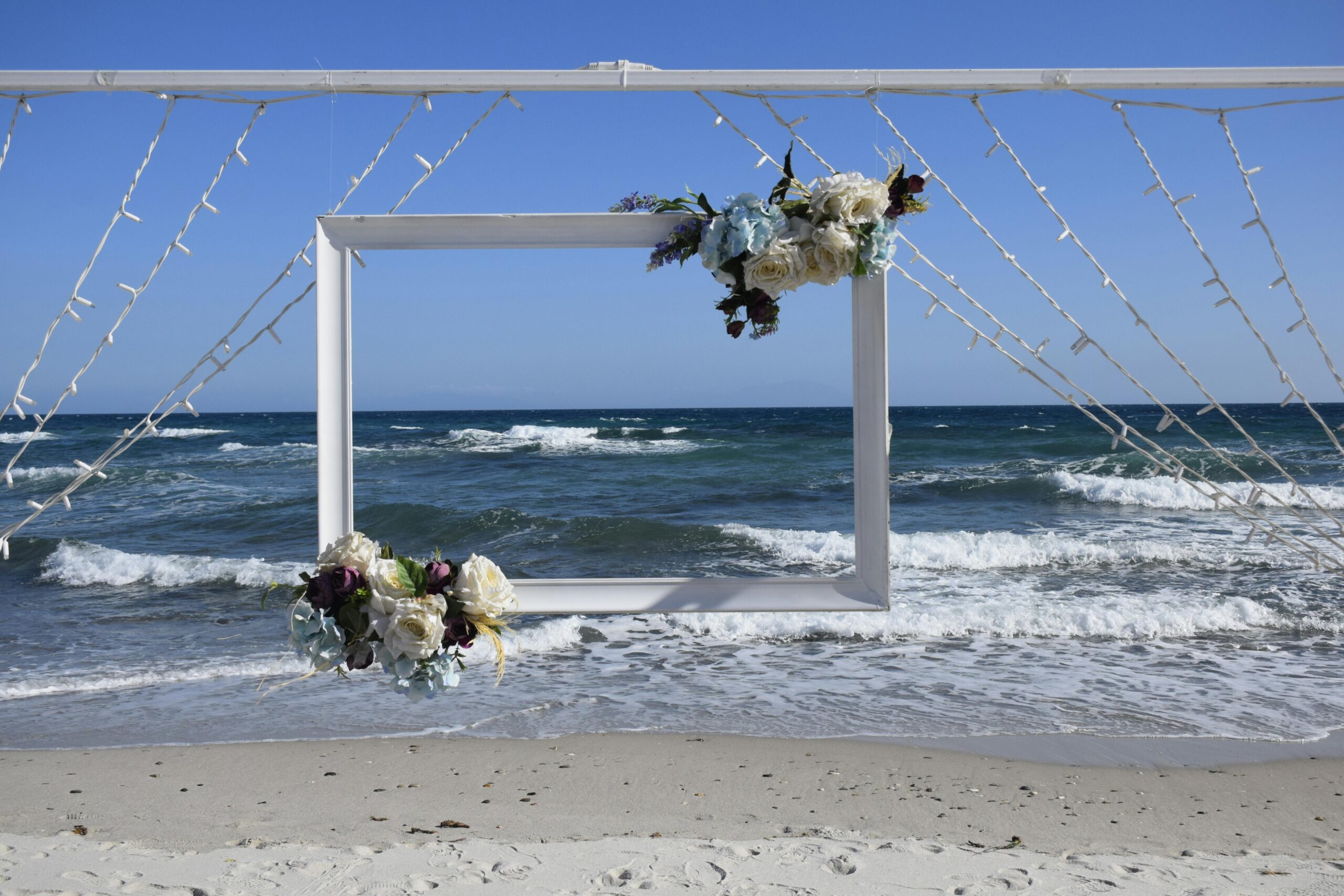 A beautiful floral wedding arch on a sandy beach with ocean waves and blue sky in Izmir, Turkey.