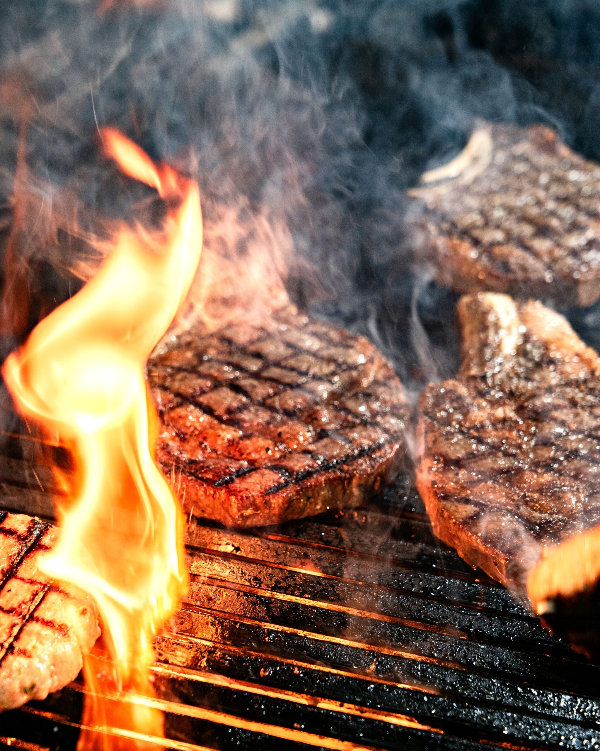 Sizzling steaks grilling over an open flame, perfect for summer barbecues and outdoor cooking themes.
